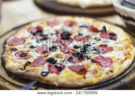 Pizza In The Pizzeria. Background Image, Blur, Blurred Frame. Pizza With Salami And Olives.