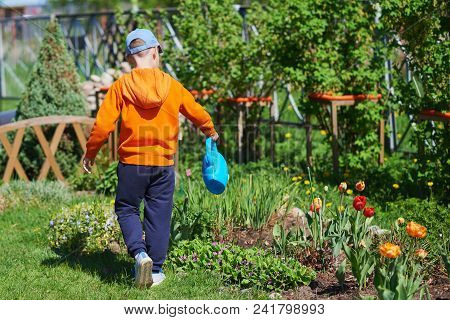 Caucasian Boy Watering Flowers With Water Can At A Household Plot. Back View.