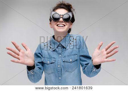 Young Girl In Black Cat Glasses On A Gray Background. Portrait Of A Young Beautiful Girl. Charming G