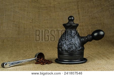 A Steel Measuring Spoon With Roasted Coffee Beans And A Made Of Black Clay сoffeepot On A Coarse Can