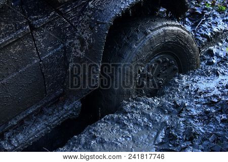 Fragment Of Offroad Car Stuck In Dirt, Close Up. Wheel In Deep Rut Goes Through Mud And Leaves Trail