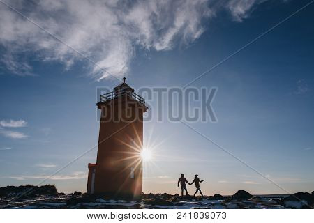 Young Couple Holding Hands And Walking Near Lighthouse In Iceland, Reykjanes, Stafnesviti