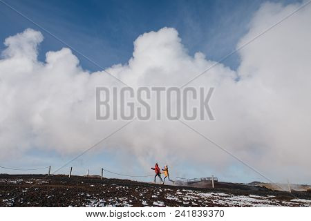 Young Couple Running Together With Steam From Geothermal Hot Springs Behind, Reykjanes, Gunnuhver Ho