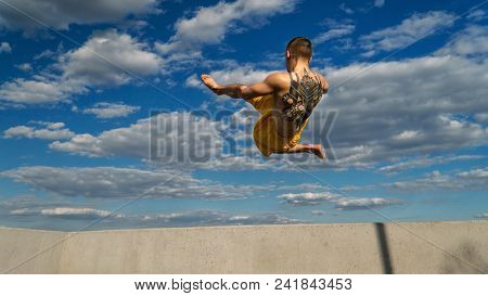 Tricking On Street. Martial Arts. Man Makes High Jump Barefoot. Shooted From Bottom Foreshortening A