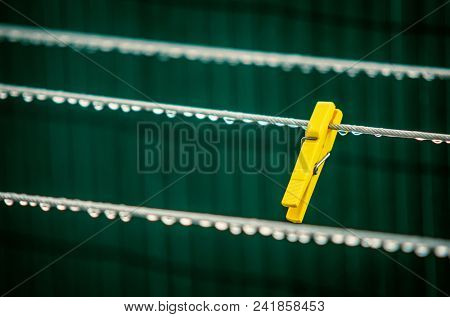 Single yellow clothes pin in a wet cord with water drops