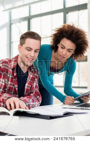 Two young students browsing internet for online useful up-to-date information while writing together an assignment in the interior of a modern university