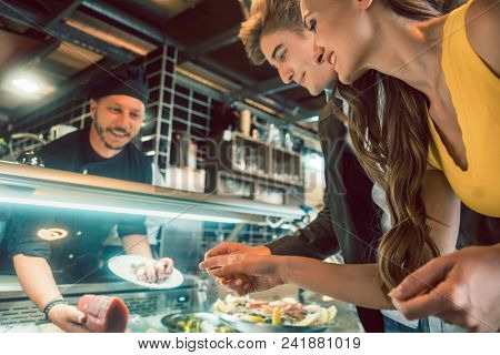 Experienced chef choosing raw seafood from the freezer for two customers in a trendy restaurant or cafeteria with fresh food