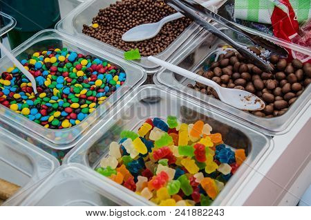 A Sample Of Several Candies In Plastic Containers: Gummies, Colored Candies, Chocolates, Etc.