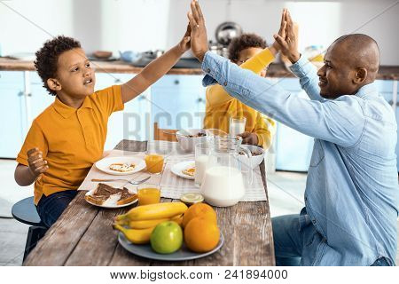 Best Team. Cheerful Single-parent Family Sitting At The Kitchen Table And Giving Each Other A High F