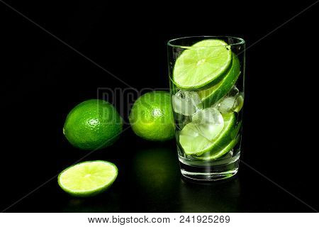 Glass With Ice And Fresh Ripe Green Limes On Black Background. Preparation Of Lemonade. Mojito Cockt