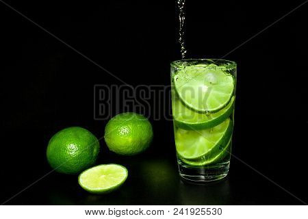 Cold Detox Water With Ice And Fresh Ripe Slice Green Limes On Black Background. Summer Refreshing An