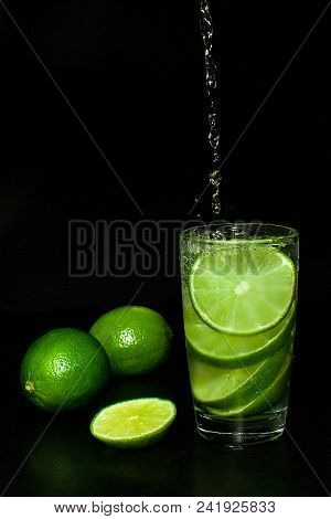 Summer Refreshing And Beverages Concept. Stream Of Water Is Poured Into Glass Of Cold Drink With Ice