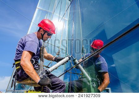 Industrial Climber Is Applying Silicone To Rubber Juncture Among Building Glass Facade.