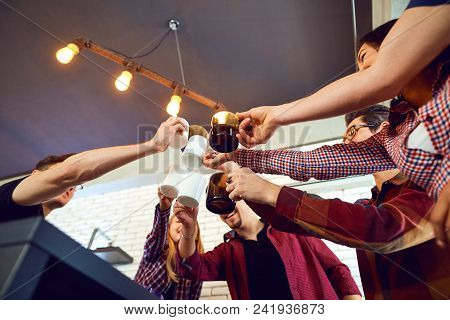 Friends Raised Their Hands Upwards With Cup Inside The Room.