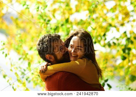 Man And Woman With Happy Faces On Autumn Trees Background. Couple In Love Cuddles And Play In Park. 