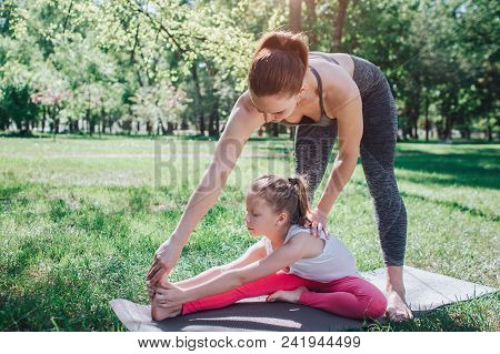 A Picture Of Woman Standing Upon Her Daughter And Teaching Her To Stretch. Small Girl Is Reacing Her