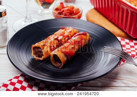 Italian Cannelloni Stuffed With Minced Meat And Served With Tomato Sauce And Red Wine On Black Plate