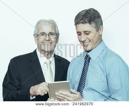 Two Positive Businessmen Using Portable Device. Successful Senior Man Looking At Camera, Middle-aged