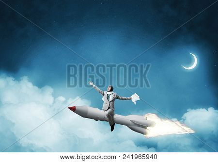 Conceptual Image Of Successful Businessman In Suit Flying On Jet Rocket With Blue Night Skyscape Wit