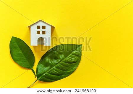 Miniature Toy Model House With Green Leaves On Yellow Colourful Trendy Backgdrop. Eco Village, Abstr