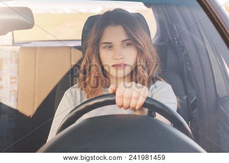 Photo Of Attractive Female Driver Sits In Car, Teaches To Drive, Being Inexperienced, Has Thoughtful