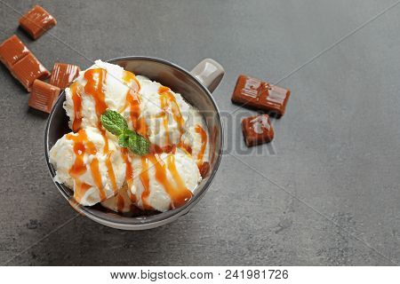 Tasty Ice Cream With Caramel Sauce In Mug And Candies On Table
