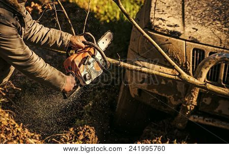 Ofroad For Hard Man. Male Hands Hold Chainsaw And Car Covered With Mud On Sunny Nature Background. S