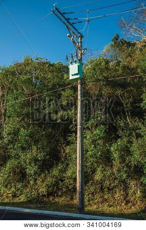High-voltage Power Pole With Transformer And Electrical Wiring On Street In Front Of Trees Near Gram