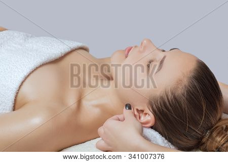 Masseur Makes A Relaxing Massage On The Ears, Face, Neck, Shoulders And Collarbones Of A Young Beaut