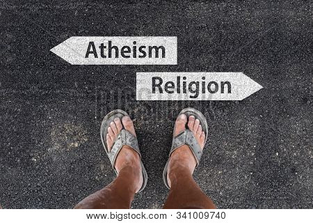 Man With Dirty Feet In Slippers Is Standing On Asphalt Next To Arrow Signs Of Words Atheism And Reli