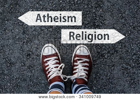 Men With A Shoes Are Standing On Asphalt Next To Arrow Signs Of Words Atheism And Religion