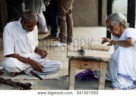 November 30, Maharashtra India, - An Elderly Man And Lady Lady In White Dress Reading Books And Sewi
