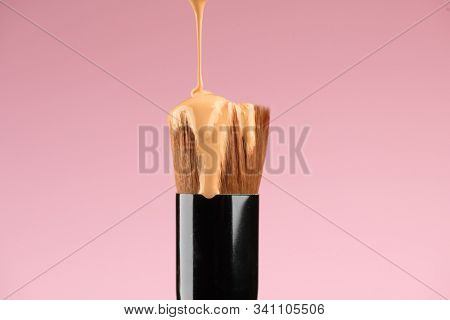 Makeup liquid foundation pouring on make-up blender sponge, closeup. Foundation beauty facial cosmetics, tool for perfect make up. Dripping bb cream or concealer, over pink background.