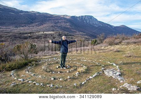 A Smiling Happy Adult Man, A Hiker, With Backpack, With His Arms Spread Wide, Stands In The Center O