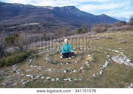 An Adult Mature Woman Practices Yoga In The Center Of A Spiral Laid Out Of Stones On The Top Of Para