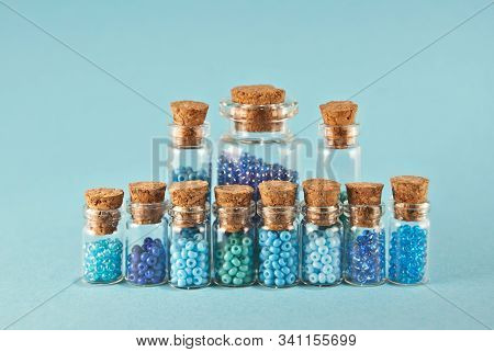 Purple And Cyan Beads In Glass Jars On Bright Blue Background. Beads In A Transparent Container With