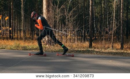 Training An Athlete On The Roller Skaters. Biathlon Ride On The Roller Skis With Ski Poles, In The H