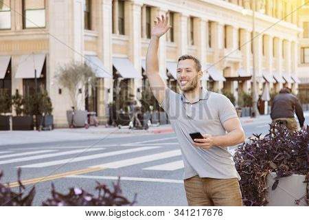 White Male With A Smile Calls For An Uber Driver While Holding His Cell Phone In The City On A Brigh