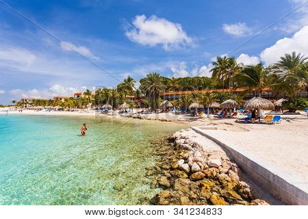 Beautiful View Of White Sand Curacao Beach. Blue Sunbeds Under Sun Umbrellas On Turquoise Water And 