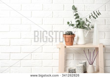 Beautiful Plants And Accessories On Wooden Shelves Near Brick Wall At Home. Space For Text