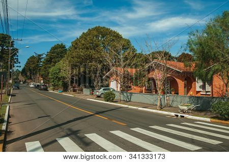 Gramado, Brazil - July 21, 2019. Gardened Houses And Trees On Empty Paved Street With Parked Cars In