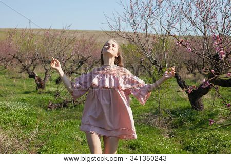 Beautiful Blonde Woman In Pink Dress Walks Through The Flowering Garden Spring