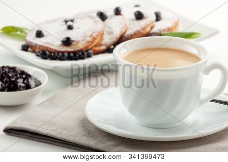 A Cup Of Coffee With Milk And A Plate With A Pancakes Is On The Table.