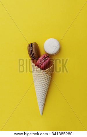 Macarons Cakes. Stil Life Photo Of Waffle Cone With Macaroons On Yellow Background. Flat Lay, Desser