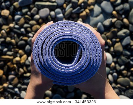 Rolled Up Yoga Mat In Women's Hands. Stones On The Beach