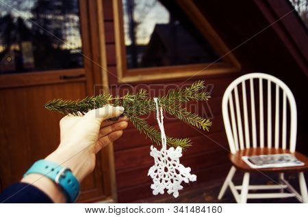 A Female Hand Holding A Fir Tree Branch With A Crochet Cnowflake Outdoors