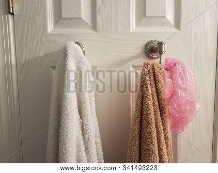 White And Brown Towel On Hook On Bathroom Door With Pink Showercap
