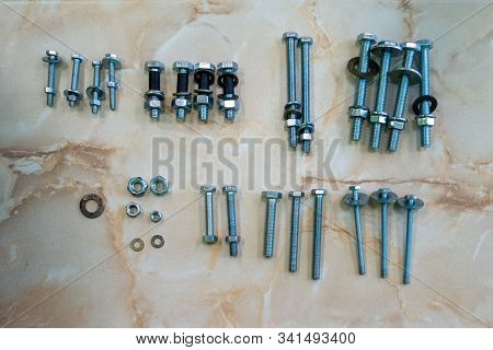 A Set Of Bolts, Washers And Nuts Of Several Diameters And Lengths Lying On A Marble-like Surface.