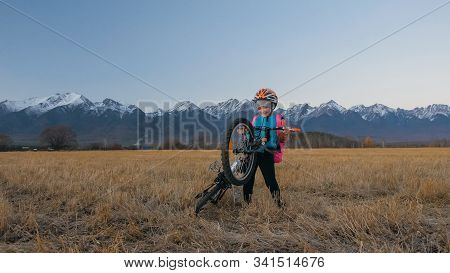 One Caucasian Children Walk With Bike In Wheat Field. Little Girl Walking Black Orange Cycle On Back
