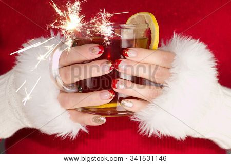 Woman With Red And Gold Nails With Golden Snowflakes Holding Cup Of Tea With Lemon And Sparkler.woma